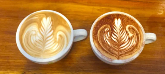 Two coffees with latte art on a timber table